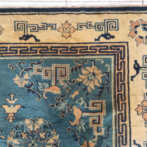 High-pile rug in teal and gold featuring intricate geometric borders and floral patterns over white tile.