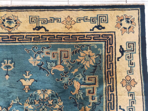 High-pile rug in teal and gold featuring intricate geometric borders and floral patterns over white tile.