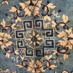 High-pile teal rug featuring a center geometric meander design and golden floral motifs.