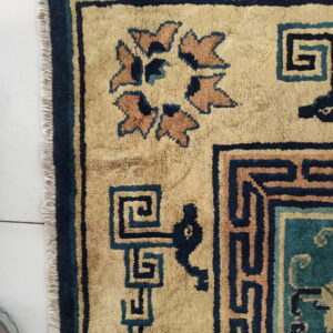 Close-up of a tan rug featuring navy and teal geometric borders and stylized rust-colored floral motifs.