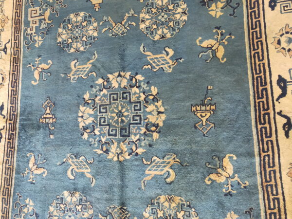 Teal rug showing stylized cream and navy medallion patterns and a wide greek key border.