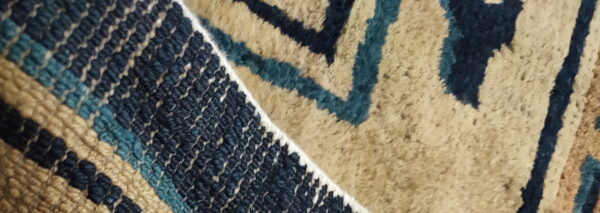 Rug detail showing a sharp division between woven flatweave and plush pile in navy, teal, and tan colors.