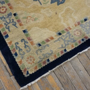 Textured beige rug featuring large floral patterns and a multicolored block border on rustic wood floors.