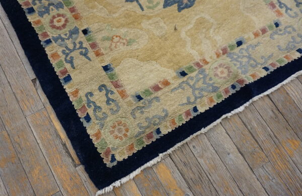 Textured beige rug featuring large floral patterns and a multicolored block border on rustic wood floors.