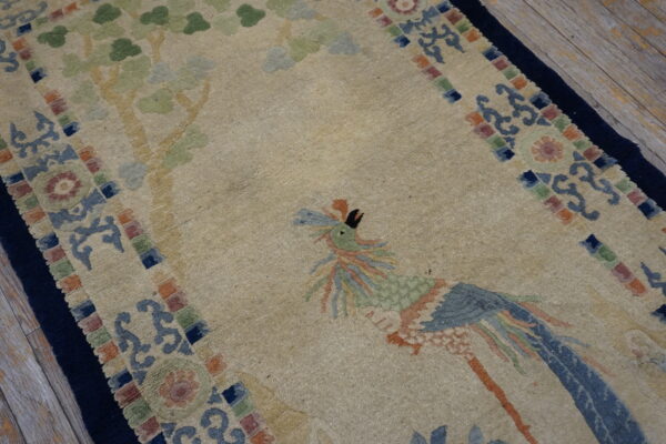 Beige pictorial rug featuring a stylized blue and green bird and soft green tree motifs on wood planks.