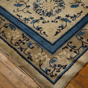 Detail of a plush beige and blue floral patterned rug corner on aged wood planks.