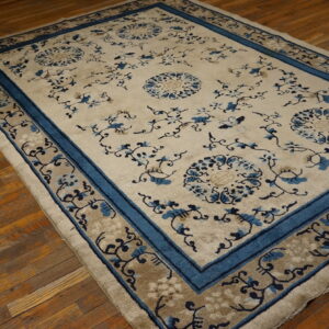 Blue and cream floral rug with layered borders lying on rustic wooden floors.