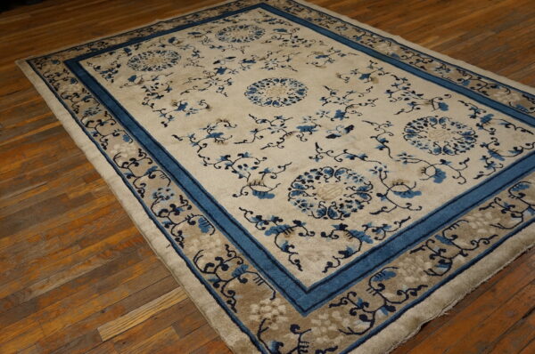 Blue and cream floral rug with layered borders lying on rustic wooden floors.