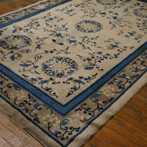 Beige rug with blue floral medallions and vines, framed by a blue border, sits on hardwood floors.