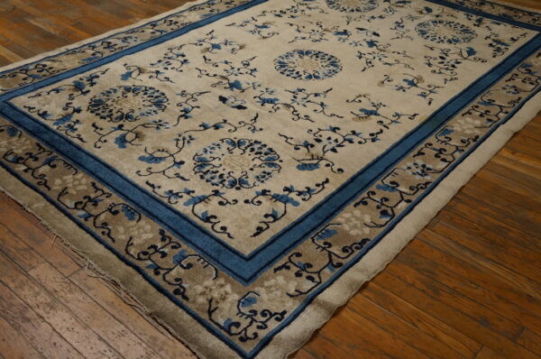 Beige rug with blue floral medallions and vines, framed by a blue border, sits on hardwood floors.