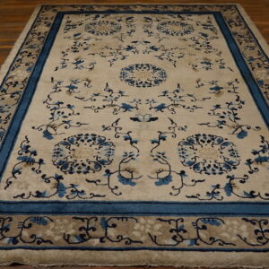 Cream rug with blue floral patterns and thick teal borders rests on dark wood flooring.