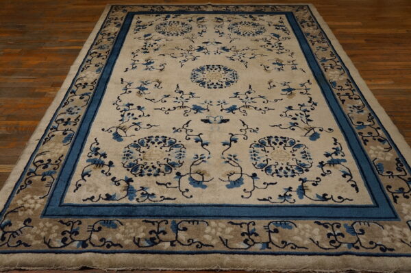 Cream rug with blue floral patterns and thick teal borders rests on dark wood flooring.