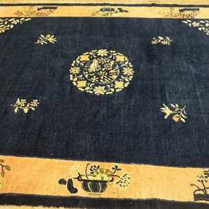 Dark blue rug with a light peach border and detailed gold botanical motifs lies on wood flooring.
