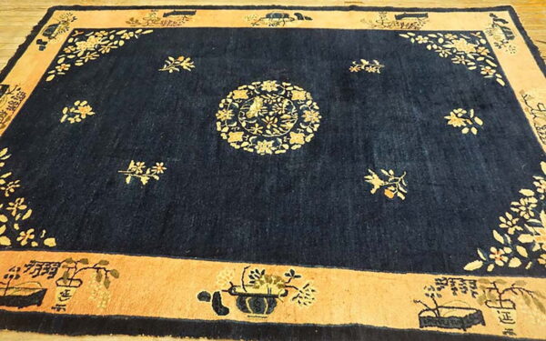 Dark blue rug with a light peach border and detailed gold botanical motifs lies on wood flooring.