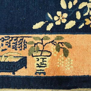 Low-pile rug section featuring a navy floral field above a peach band with stylized potted plant motifs.