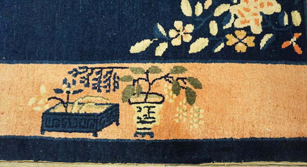 Low-pile rug section featuring a navy floral field above a peach band with stylized potted plant motifs.