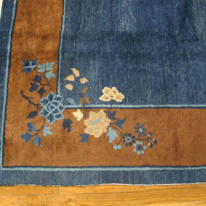 Navy blue and rust rug corner with blue and tan floral motifs rests on light wood plank flooring.