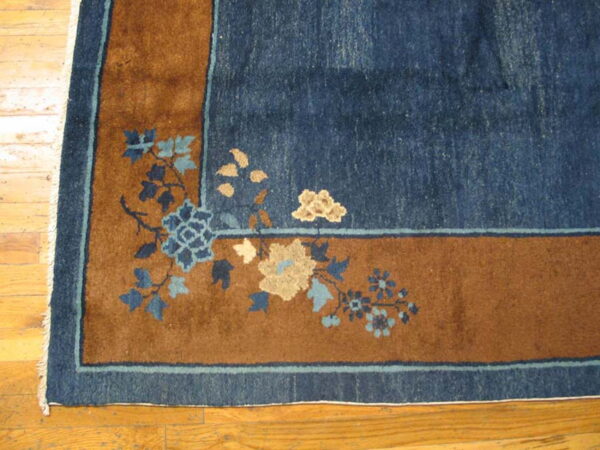 Navy blue and rust rug corner with blue and tan floral motifs rests on light wood plank flooring.