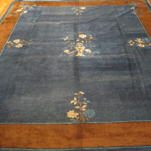 A deep blue rug features light floral motifs, a central vase design, and a contrasting wide brown border.