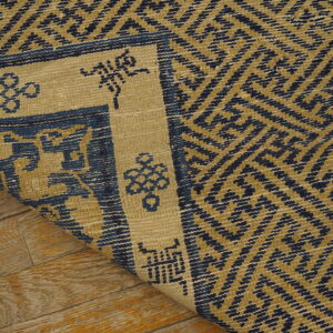 Close-up of a tightly woven blue and mustard-toned rug with a geometric design on wood floor.