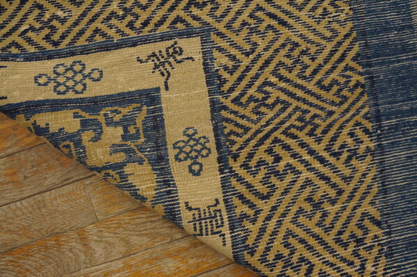Close-up of a tightly woven blue and mustard-toned rug with a geometric design on wood floor.