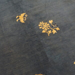 A dark blue rug displays scattered gold botanical and stylized animal silhouettes on a low-pile field.