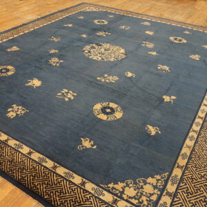 An indigo blue rug features scattered tan medallions and a detailed Greek key border on light wood flooring.