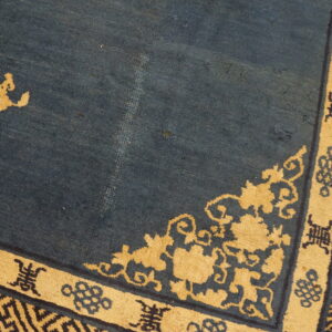 Close-up of a dark blue rug with gold floral corner motifs and geometric key pattern borders.
