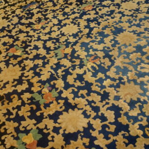 Textured high-pile rug with golden floral scrolls on a dark blue background, accented by small green and orange motifs.