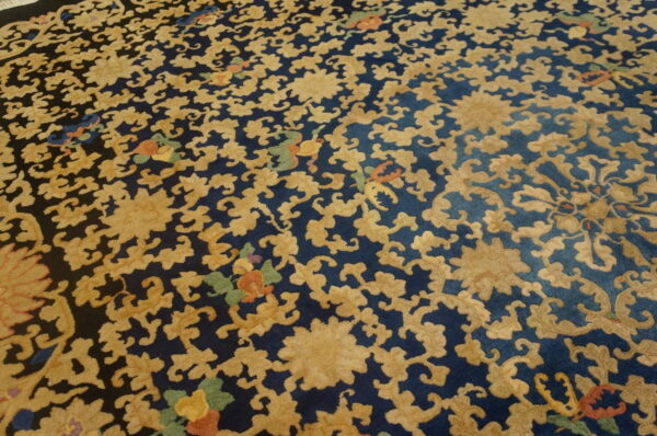 Textured high-pile rug with golden floral scrolls on a dark blue background, accented by small green and orange motifs.