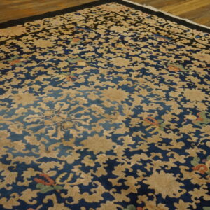 Intricate blue rug with dense gold scrolling floral patterns and a thin black border on wood flooring.
