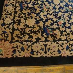 Navy and black rug featuring tan floral motifs and colorful accents on distressed yellow hardwood flooring.