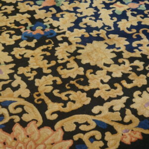 Detailed view of a textured rug featuring scrolling gold floral motifs and colorful accents on a dark field.