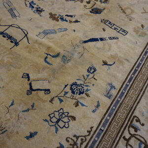 Low-pile beige rug with scattered blue and brown stylized motifs and a geometric Greek key border.