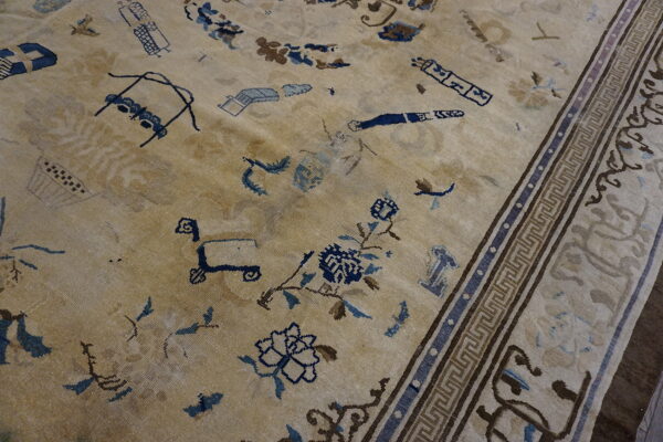 Low-pile beige rug with scattered blue and brown stylized motifs and a geometric greek key border.