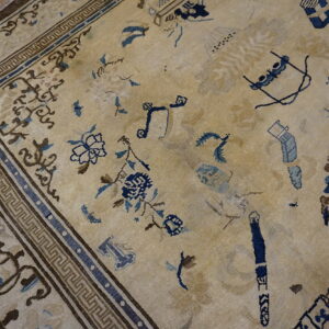Low-pile beige rug with faded brown and blue abstract motifs resting on light wood flooring.