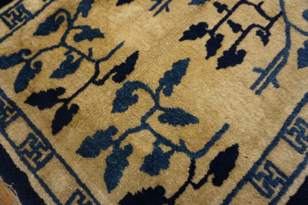 Close-up showing a plush golden tan rug with dark blue stylized floral designs and a geometric border.
