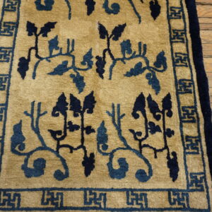 Tan rug featuring dark blue winding vines and a geometric fret border on distressed wood planks.