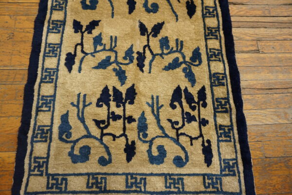 Tan rug featuring dark blue winding vines and a geometric fret border on distressed wood planks.