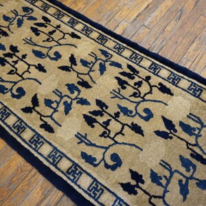 Beige and navy blue runner with intricate vine patterns and geometric border on distressed wood flooring.