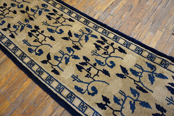 Beige and navy blue runner with intricate vine patterns and geometric border on distressed wood flooring.