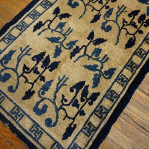 A golden tan rug with dual-tone blue vines and a key pattern border lies on rustic wood flooring.