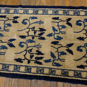 Close-up of a tan rug with dark blue vine patterns and Greek key borders on wood planks.