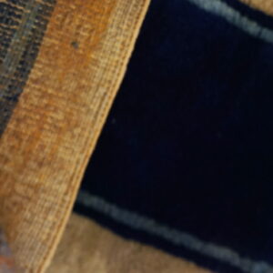 Close-up of a rug with dark navy pile and golden brown textured stripes lying on wood flooring.
