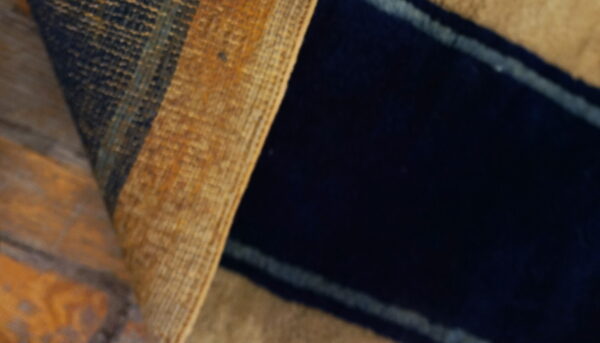 Close-up of a rug with dark navy pile and golden brown textured stripes lying on wood flooring.