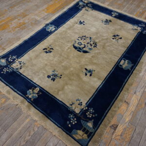 Khaki low-pile rug with blue floral motifs and a wide navy border on worn wood plank flooring.
