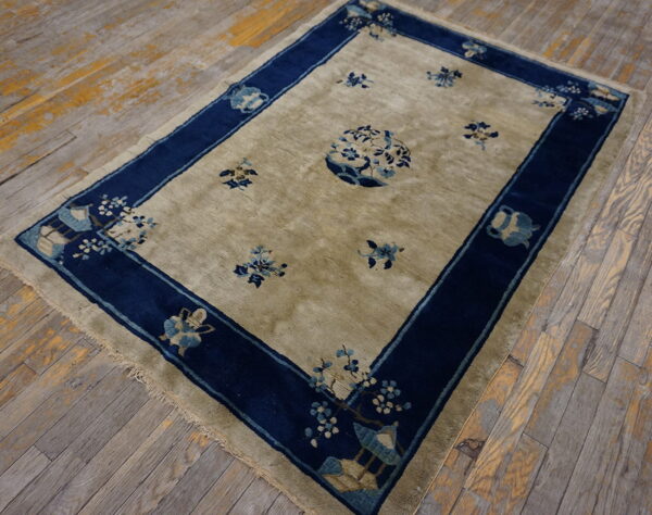 Khaki low-pile rug with blue floral motifs and a wide navy border on worn wood plank flooring.