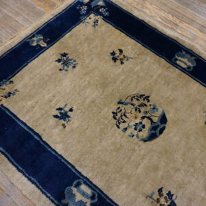 Beige rug with blue floral pattern and wide navy border rests on distressed wooden floorboards.