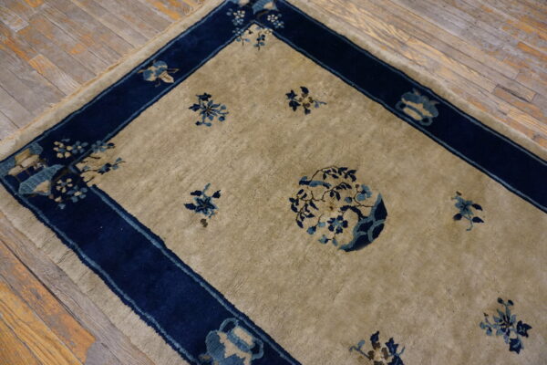 Beige rug with blue floral pattern and wide navy border rests on distressed wooden floorboards.