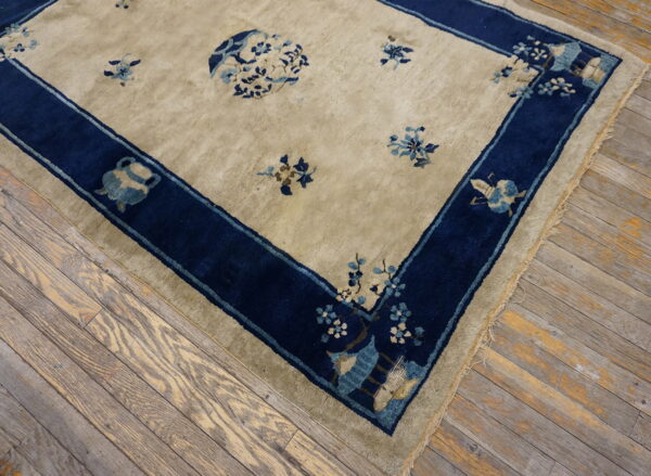 Beige rug with dark blue border and floral motifs lying on distressed wood planks.
